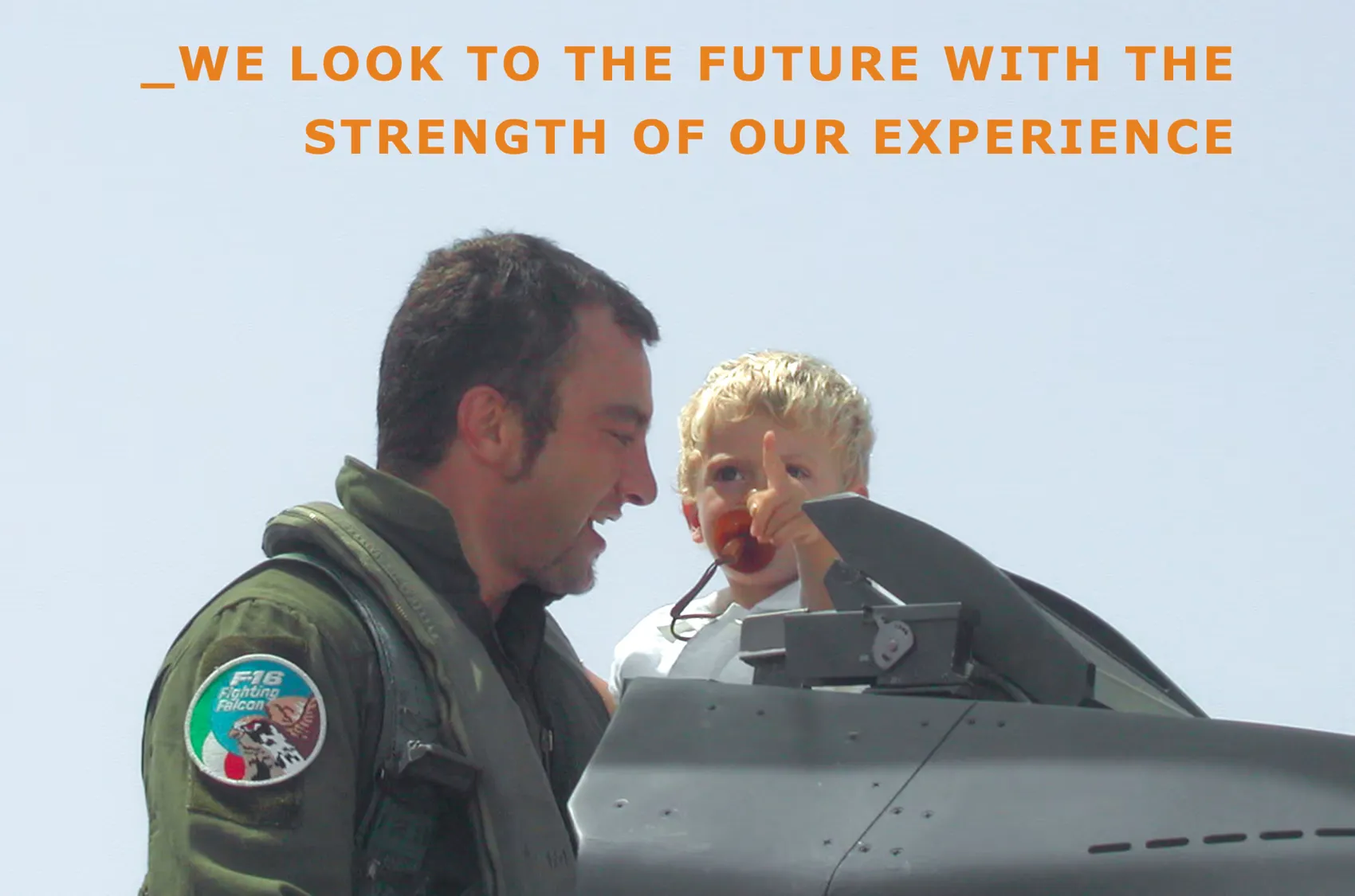 Fabio Masci, founder of THE EDGE COMPANY, in his Air Force flight suit holding a child at the cockpit of an F-16, under the line: we look to the future with the strength of our experience
